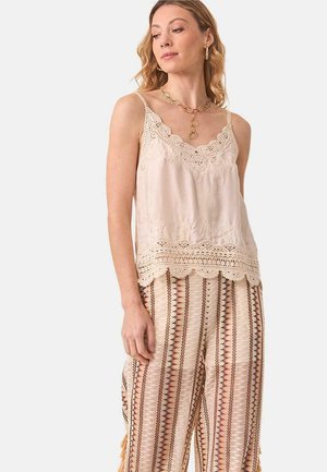 Camiseta sin mangas color beige claro con encaje en el escote y el dobladillo, combinada con pantalones de pierna ancha estampados que presentan diseños geométricos en tonos terrosos.