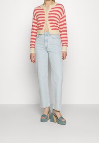 Pruhovaný kardigan v růžové a krémové barvě, měkký materiál, zkrácený střih; spárovaný s světle modrými rovnými džíny a tyrkysovými vysokými platformovými botami.