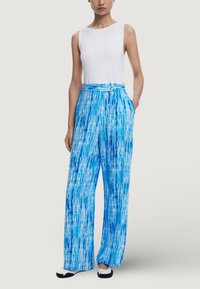 Débardeur blanc à côtes sans manches associé à un pantalon léger taille haute au motif tie-dye bleu et blanc. Le pantalon est doté de poches latérales.