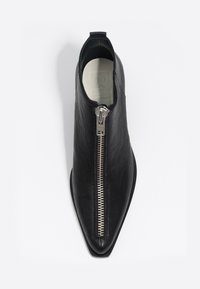 Botín de cuero negro hasta el tobillo con punta afilada, cremallera lateral y textura suave. Diseño minimalista sin adornos visibles.