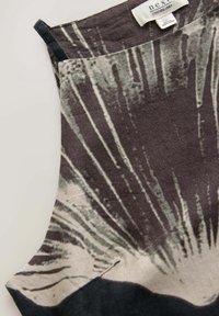 Haut sans manches en lin avec un motif radial abstrait gris foncé et clair, et une bretelle noire sur un fond clair.