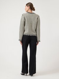 Czarna i biała kurtka w desenie z frędzlami na dole, zaokrąglonym dekoltem i długimi rękawami, zestawiona z czarnymi, szerokimi spodniami i szpilkami.