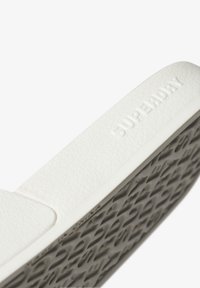 White rubber slide sandal with textured upper and patterned grey outsole. Features embossed branding along the side for added detail.