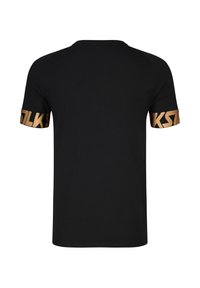 Camiseta negra de manga corta con letras doradas audaces alrededor de los puños de ambas mangas, vista desde atrás.