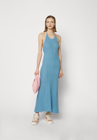 Robe maxi à côtes bleu clair avec col halter, associée à une pochette rose et des baskets montantes décoratives avec des motifs colorés.