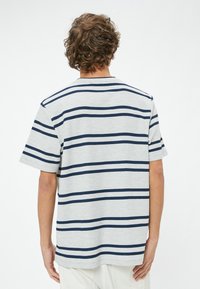 Grå och marinblå randig kortärmad skjorta med en avslappnad passform, ribbad halsringning och texturerad tyg synlig från bakvyn.