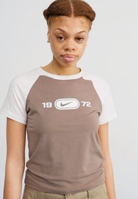 Ruda ir balta trumpomis rankovėmis marškinėliai su Nike logotipu ir numeriais "1972" ant priekinės dalies. Pagaminti iš minkštos, lygaus audinio.