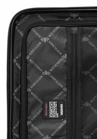 Interior de maleta negra con tejido de marca, que presenta una textura suave y un bolsillo de malla con cremallera. Etiqueta de cuidado en la esquina inferior.