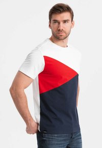 Camiseta de algodón para hombre con mangas cortas. Presenta un diseño a bloques de color: parte superior blanca, franja diagonal roja y sección inferior azul marino.