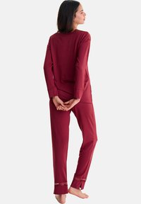 Ensemble de loungewear bordeaux comprenant des manches longues et un pantalon. Tissu doux, coupe décontractée et finitions soignées aux poignets et à l'ourlet. Design minimaliste.
