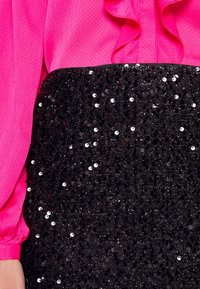 Blouse fuchsia avec un col à volants et des manches larges, associée à une jupe noire à sequins ornée de sequins circulaires brillants.