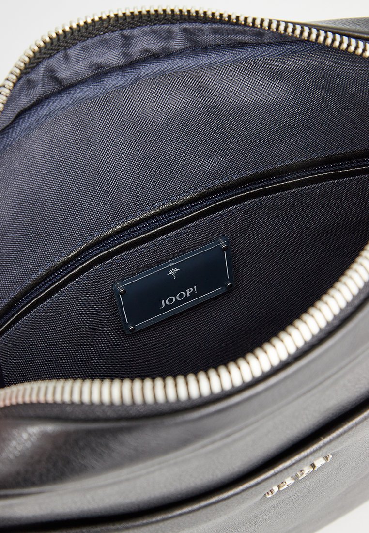 Schwarze Lederhandtasche mit Reißverschluss, ausgestattet mit einem glatten Textilfutter und einem blauen Etikett mit der Aufschrift "JOOP!" im Inneren.
