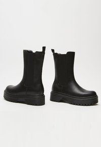 Black ankle boots with elastic side panels, round toe, chunky rubber sole, smooth leather texture, and pull tab at the back.