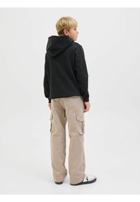 Svart huva sweatshirt, beige cargo-byxor med sidofickor, och svarta sneakers. Enkla bakgrund med minimal textur.