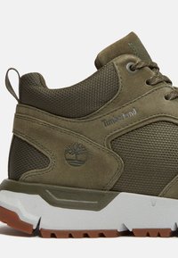 Zapatillas de deporte verdes de ante y malla con una superficie texturizada, cordones redondos, logo de Timberland y una suela de goma blanca con acentos marrones.
