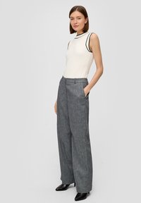 Haut blanc sans manches avec des accents noirs, associé à un pantalon large taille haute gris. Les pantalons présentent une texture subtile et des poches latérales.