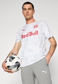 Gray camouflage-patterned t-shirt with red "Red Bull" logo and Puma branding, paired with gray pants. Holding a black and white soccer ball.