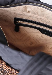 Open zwarte gestikte tas met een beige binnenvoering waarin de herhaalde tekst "CAFE NOIR" staat en een klein ritszakje met zwarte randen.
