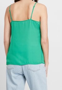 Camisole verte légère avec bretelles spaghetti réglables et ourlet droit. Texture lisse, coutures minimales, sans motifs visibles.