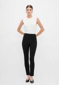 Un haut sans manches blanc avec un col rond associé à un pantalon noir ajusté, créant une silhouette fluide. Des ballerines noires complètent le look.