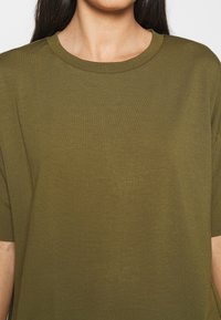Oliwkowy t-shirt z krótkim rękawem, okrągły dekolt, wykonany z gładkiego materiału, o luźnym kroju z subtelnymi detalami w szwie.