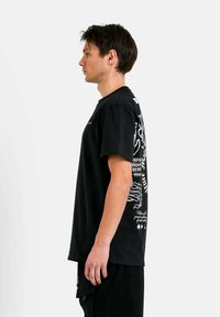 Zwarte katoen t-shirt met witte grafische ontwerpen op de achterkant en de linkermouw. Standaard pasvorm, korte mouwen en ronde hals.