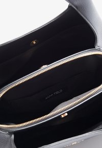 Borsa a tracolla in pelle nera con hardware dorato, chiusura con zip e interno foderato in tessuto. Presenta una tasca interna con etichetta "ANNA FIELD".