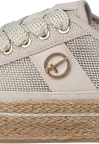 Baskets beiges avec une semelle épaisse en jute tissé, une tige en tissu texturé, des lacets épais tressés et un logo circulaire doré sur le côté.