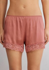 Rosaröda shorts i mjukt tyg med en scallopad spetsdetalj vid fållen. Elastisk midja för komfort och passform.