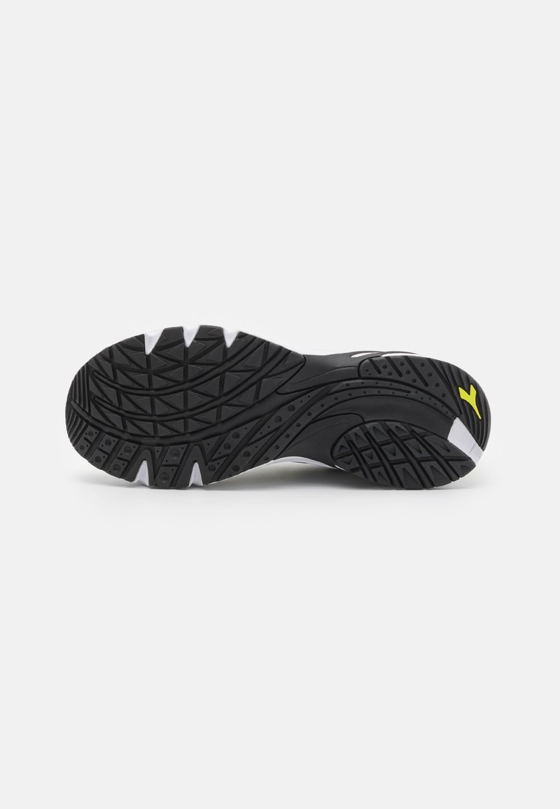 Zwart-witte sneakerzool met getextureerde grippatronen en een klein geel logo op de hiel, geplaatst tegen een effen witte achtergrond.