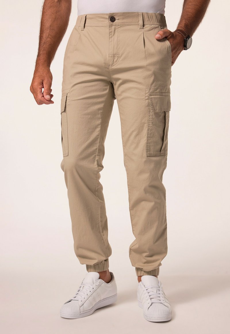 Beige cargo bukser med elastiske mansjetter, der har sidelommer og knaplukning. Lavet af tekstureret stof. Sættes sammen med hvide sneakers.