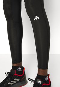 Czarne legginsy sportowe o gładkiej fakturze z białym logo w trzy paski. W połączeniu z czarnymi sneakersami z czerwonymi akcentami.