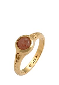 Aranyozott gyűrű, sima foglalatba helyezett kerek narancssárga kővel. Díszes gravírozással ellátott, texturált szalaggal rendelkezik, és 925 Ag jelöléssel van ellátva.