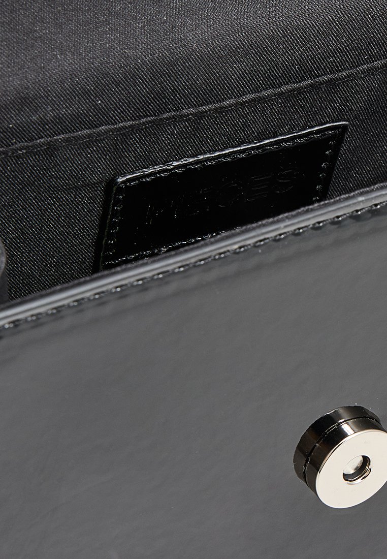 Gros plan sur l'intérieur d'un sac à main en cuir noir montrant un revêtement en tissu cousu, une petite étiquette de marque noire et un fermoir magnétique argenté.
