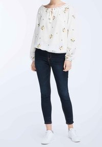 Blusa floreale bianca con scollo arricciato e dettaglio con cordoncino abbinata a jeans skinny blu scuro e sneakers bianche.