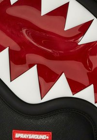 Mochila negra con un diseño de boca de tiburón rojo y blanco brillante. Superficie texturizada con un prominente logo rojo en la parte inferior.
