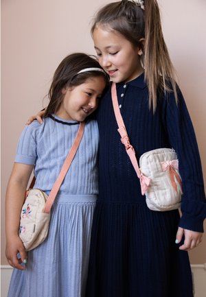 Two girls in knitted dresses, one in light blue and one in navy, embrace while wearing small quilted crossbody bags with pink straps.