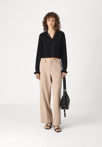 Melna īsā kardigāna ar mežģīņu apmalēm un pogām, bēšas platās bikses un melni sandaļi ar siksniņām. Melna rokassoma ar plecu siksnu.