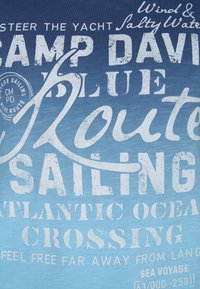 Texte sur un tissu bleu avec des phrases liées à la voile et à la navigation : « Camp David », « Route », « Voile », « Traversée de l'océan Atlantique » et « Voyage en mer ».