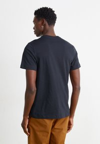 T-shirt de algodão preta com mangas curtas, apresentando um decote redondo. A vista traseira mostra uma textura suave e um corte relaxado.