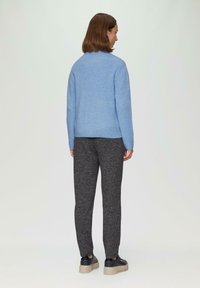 Hellblaues Strickpullover mit geripptem Muster, kombiniert mit dunkelgrauen, strukturierten Hosen. Schwarze Schuhe mit dicken, hellen Sohlen.
