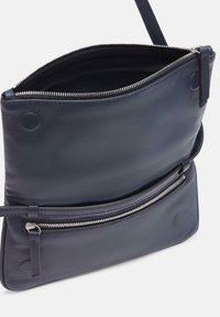 Granatowa skórzana torba na ramię z zamkiem błyskawicznym na górze i przednią kieszenią. Posiada gładką fakturę i minimalne detale metalowe.