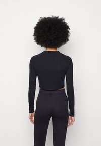 Black, long-sleeve cropped top made of a soft, stretchy fabric with a rounded neckline and raglan sleeves, paired with matching black pants.