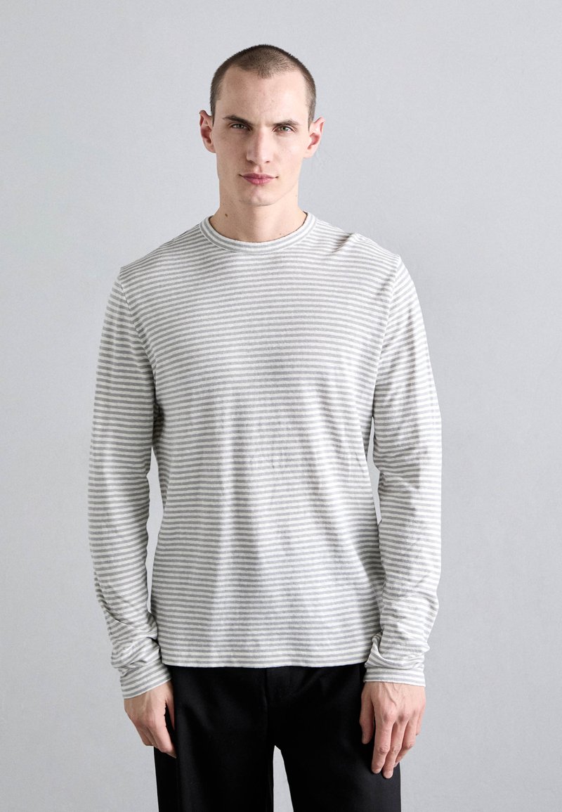 Camisa gris de manga larga con finas rayas blancas, hecha de una tela suave con cuello redondo y puños ajustados, combinada con pantalones negros.