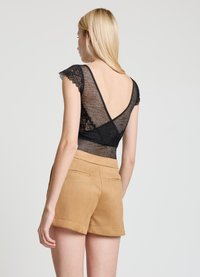 Black lace bodysuit with cap sleeves, deep V-back design, paired with tan, tailored shorts featuring back pockets and smooth texture.
