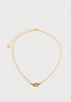 Finom dupla aranylánc nyaklánc ovális alakú medállal, amely apró, tiszta kristályokkal van kirakva, és egy kis háromszög alakú dísz a kapocs közelében.