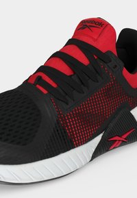 Μαύρο και κόκκινο αθλητικό παπούτσι Reebok με άνω μέρος από πλέγμα, μαύρα κορδόνια, λογότυπο στη γλώσσα και λευκή υφασμένη σόλα, με κλίση για να εμφανίζονται οι λεπτομέρειες από το πλάι και από πάνω.