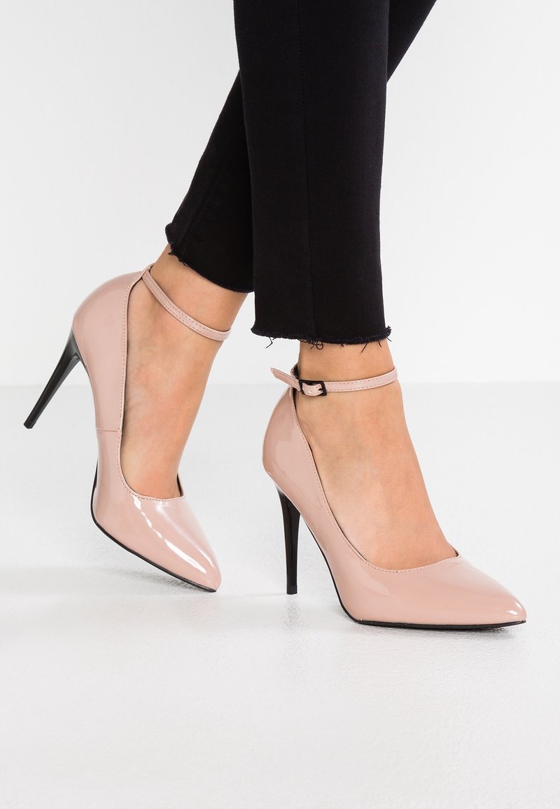 Escarpins nude en cuir verni avec bout pointu et bride à la cheville, dotés d'un talon fin noir et d'une finition lisse et brillante.
