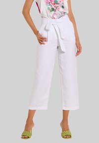 Weiße Leinen-Hose mit weitem Bein und einem taillierten Gürtel, kombiniert mit grünen, geflochtenen Sandalen mit Blockabsatz. Ein floral bedrucktes Oberteil verleiht einen lebendigen Akzent.