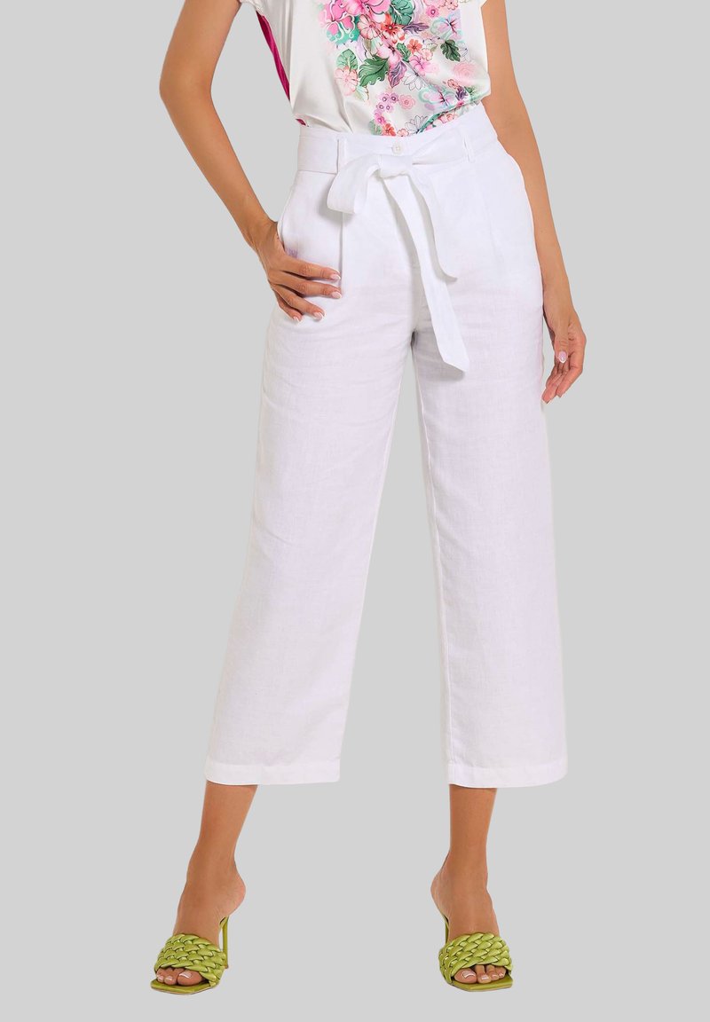 Weiße Leinen-Hose mit weitem Bein und einem taillierten Gürtel, kombiniert mit grünen, geflochtenen Sandalen mit Blockabsatz. Ein floral bedrucktes Oberteil verleiht einen lebendigen Akzent.